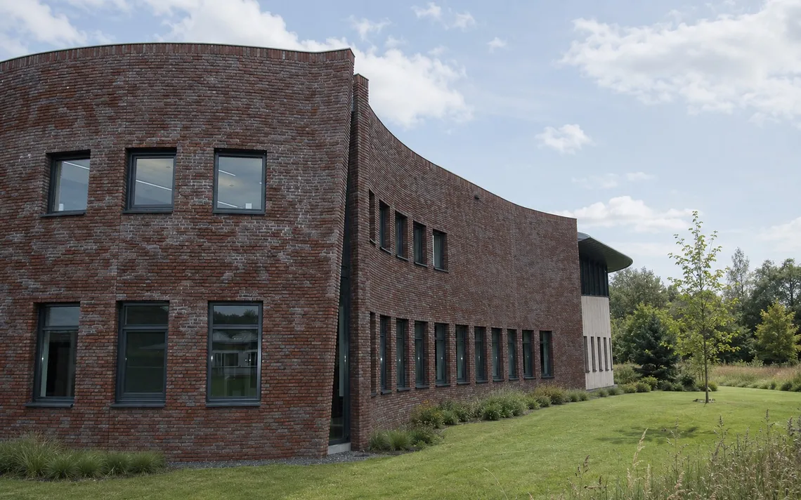 Bakstenen gevel van het ProWonen-kantoor met hoge ramen en groene buitenruimte.